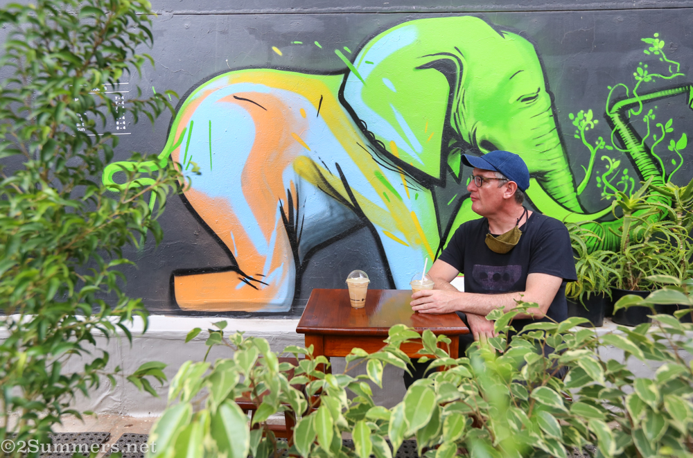 Thorsten at JFF Rooftop with the Falko mural and his iced coffee
